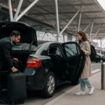 Suited taxi driver unloading passenger luggage from a car at Heathrow Airport Departures