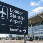 London Stansted Airport terminal with a large directional sign pointing towards the terminal entrance. Stansted drop-off charges.