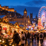 Festive UK Christmas market at dusk, with illuminated wooden stalls, a Ferris wheel, Christmas tree and visitors enjoying Christmas shopping.
