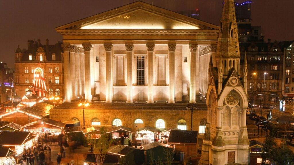 Birmingham Christmas Market: Illuminated Christmas market stalls in Birmingham's Victoria Square, with the Town Hall and Chamberlain Memorial at night.