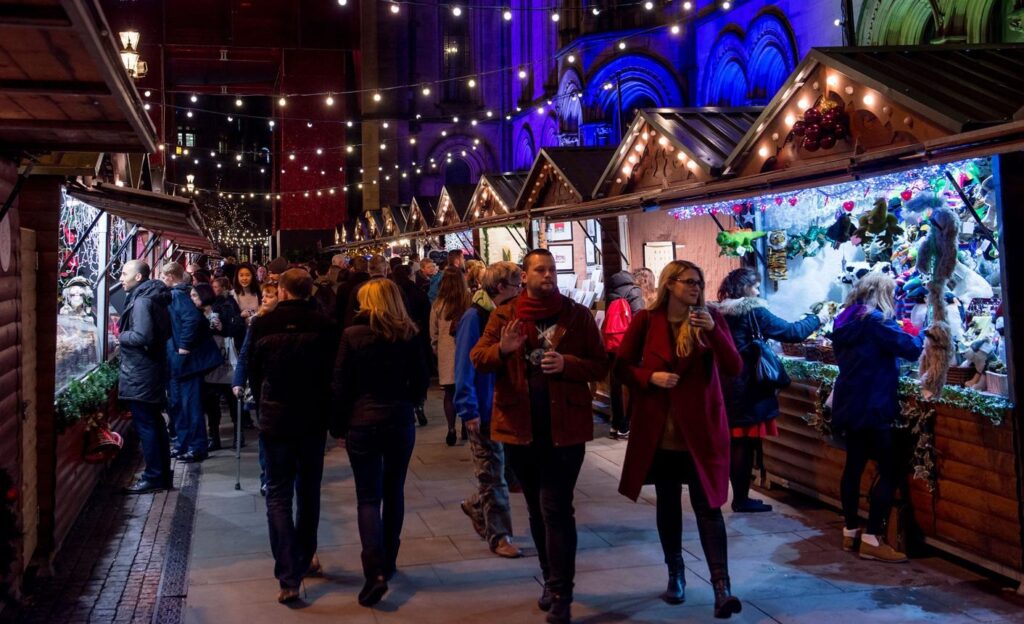 Manchester Christmas Markets: Wooden Christmas market stalls decorated with festive lights in Manchester city centre.
