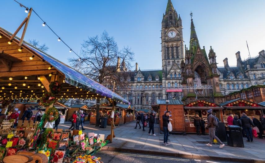 Manchester Christmas Market - busy market stalls with a church and clock tower in the background